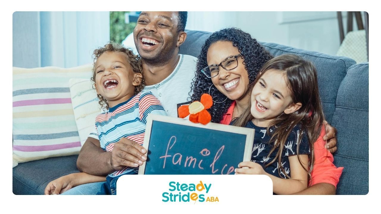 Family sitting on couch with autistic children, smiling, holding chalkboard sign that says “family.”