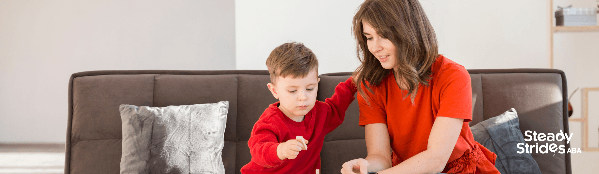 A female therapist and autistic boy playing with wooden blocks together on a couch at home.