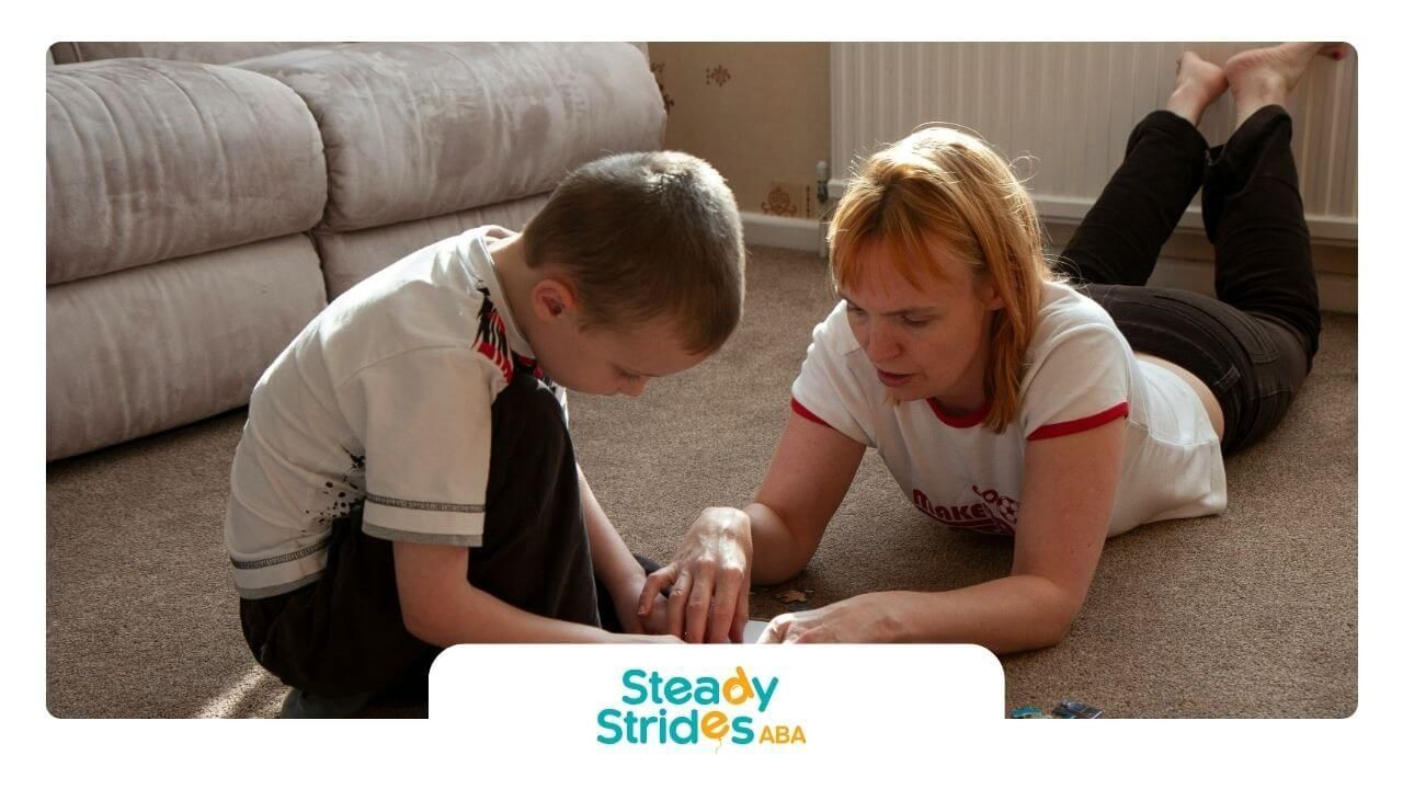 ABA Therapist and autistic child work on jigsaw puzzle on carpeted floor in cozy living room.