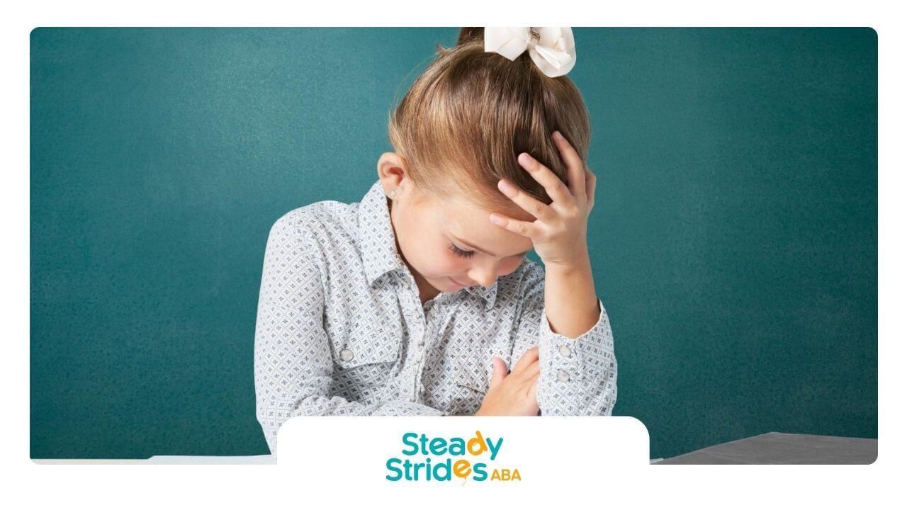 Young girl with autism sitting at a desk with her head in her hand looking frustrated.