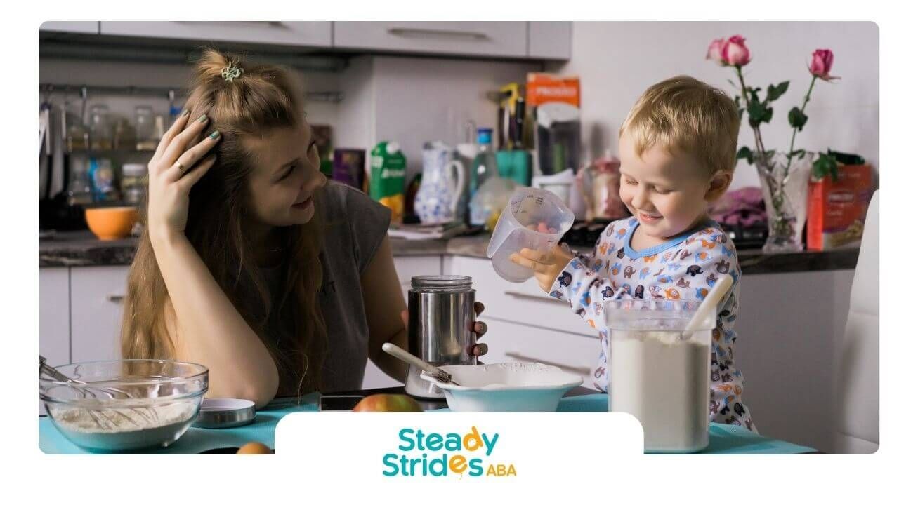 Therapist and autistic boy baking in the kitchen, smiling while pouring ingredients into a bowl.
