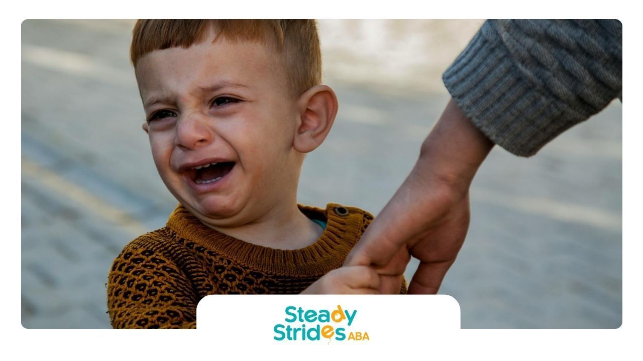 Young child with autism crying while holding an adult’s hand outdoors on a paved path In Texas.