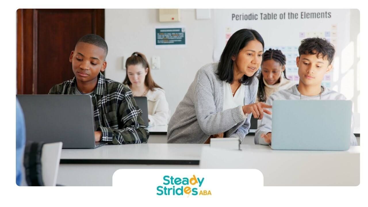 Therapist assisting middle school students working on laptops in the classroom during academic.