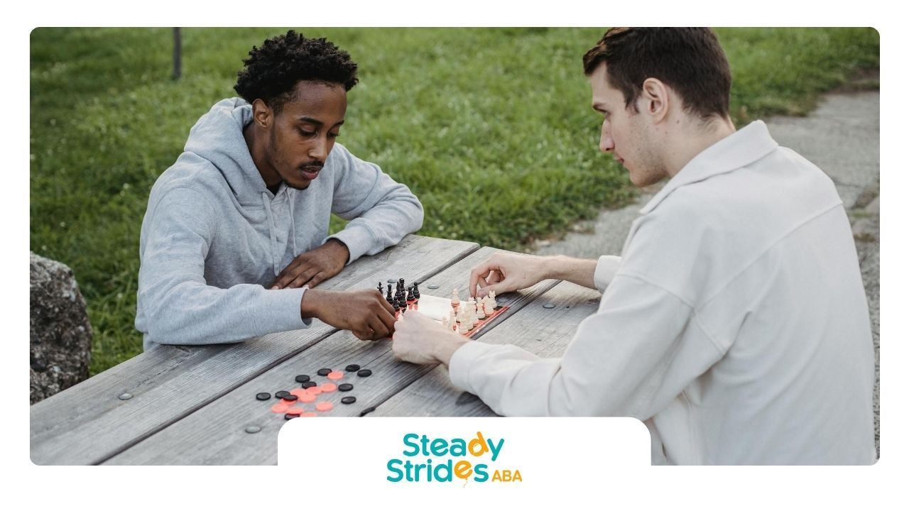 Two men with autism playing chess board game outdoors on a picnic table at a park in Texas.