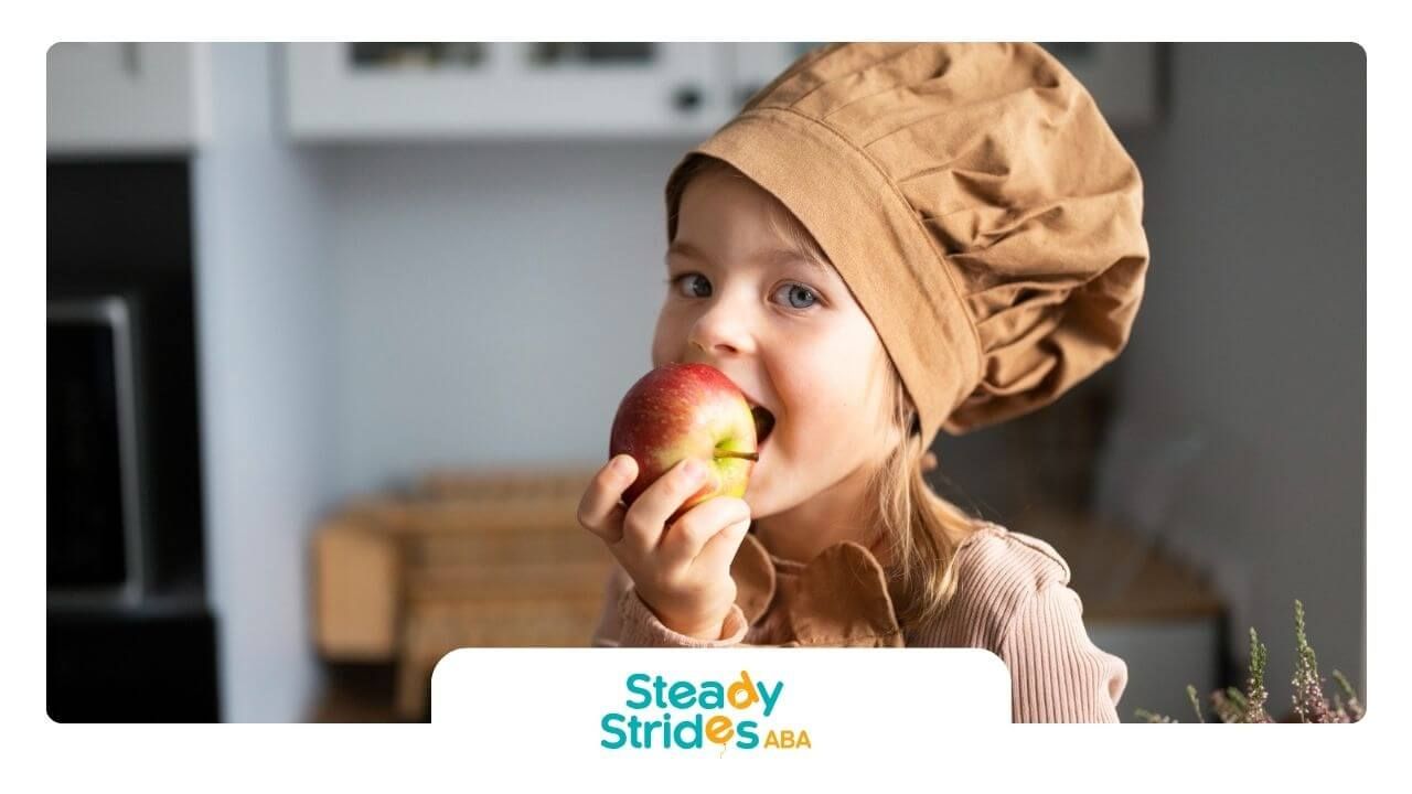 A girl with autism wearing a chef's hat is eating an apple.