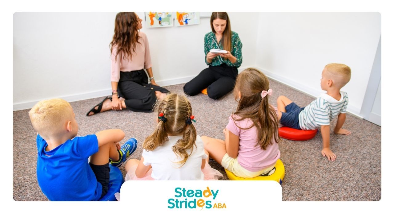 A group of children are sitting in a circle on the floor while a teacher reads a book.