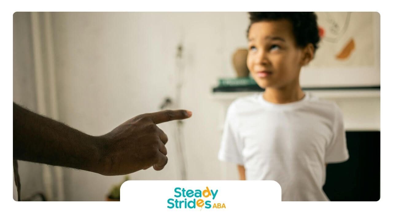 A child standing with a parent pointing at them, appearing in a discipline or corrective moment.