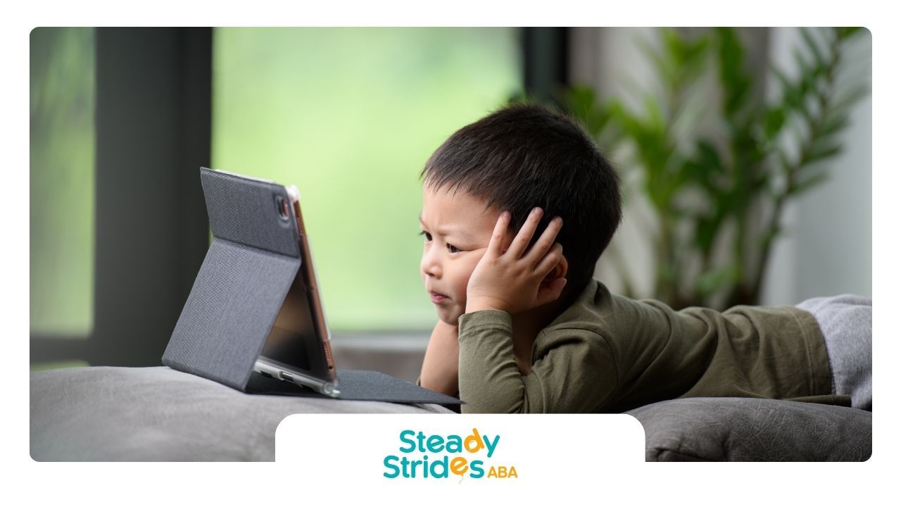 A young boy is laying on a couch looking at a tablet.