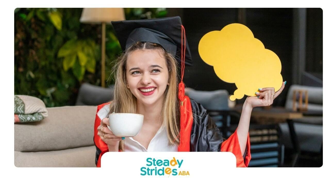 Smiling ABA in cap and gown holding coffee and a speech bubble sign, celebrating academic success.