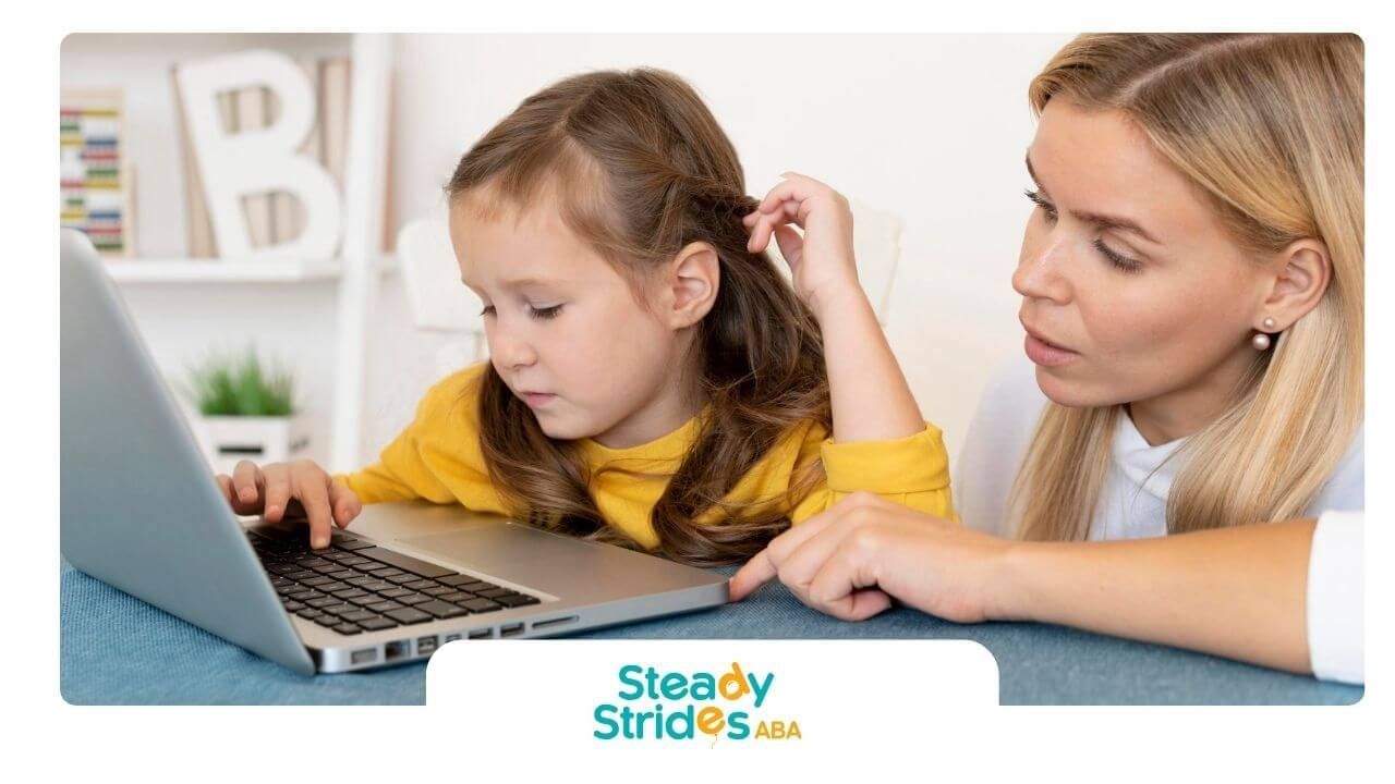 Therapist guiding autistic girl while they look at a laptop screen together on a couch at home.