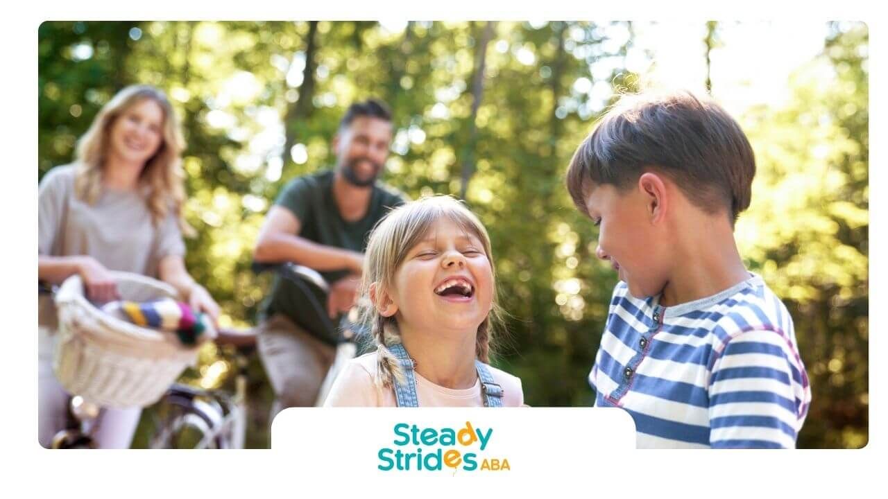 Autistic children laughing and playing outdoors with therapist nearby, promoting social skills.