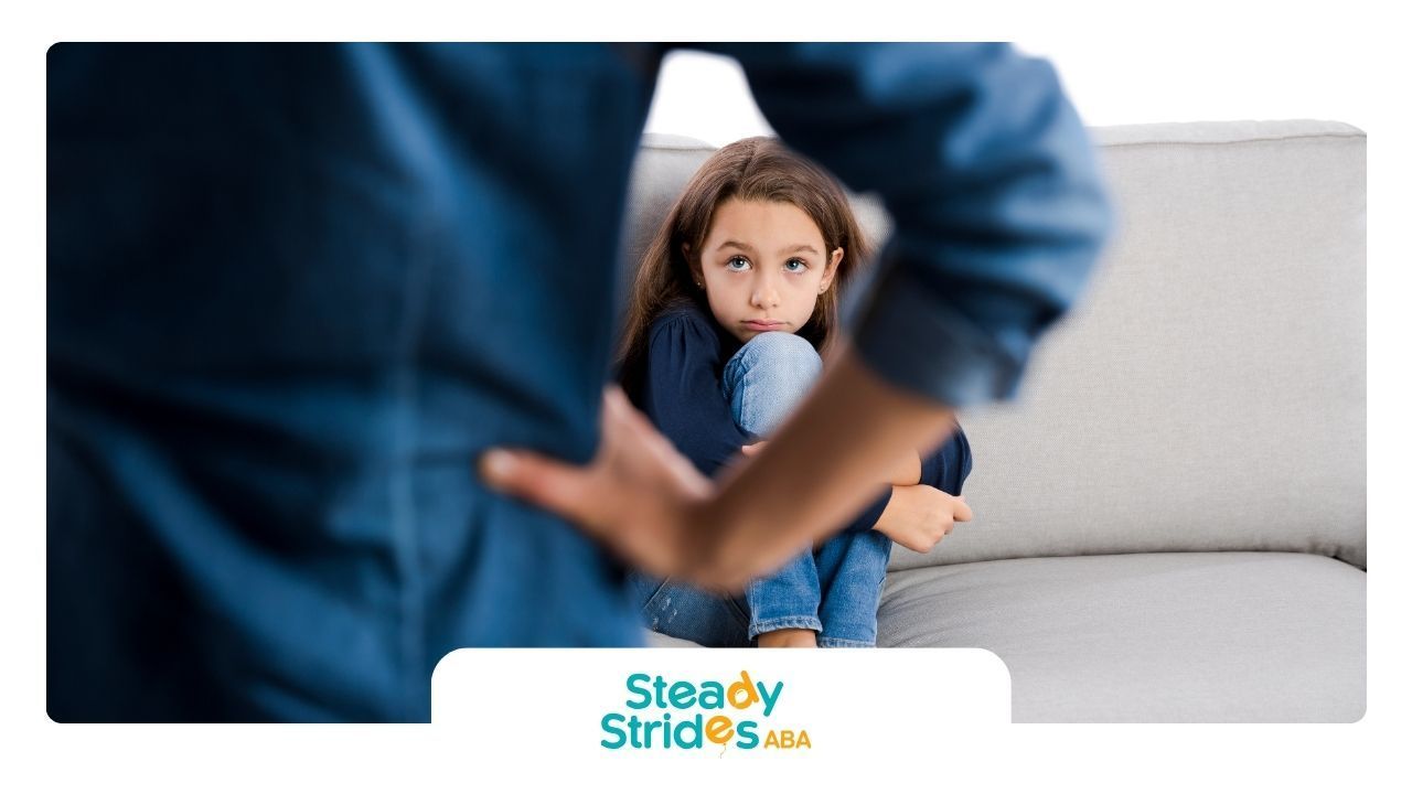 A man is standing next to a little girl who is sitting on a couch.