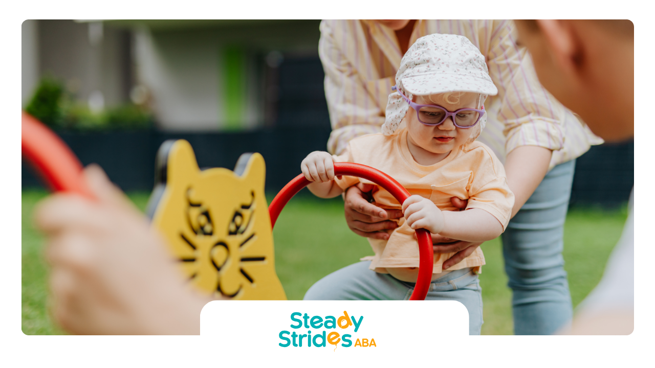 Child on playground ride, assisted by an adult. Bright yellow seesaw. The child wears glasses and a hat.