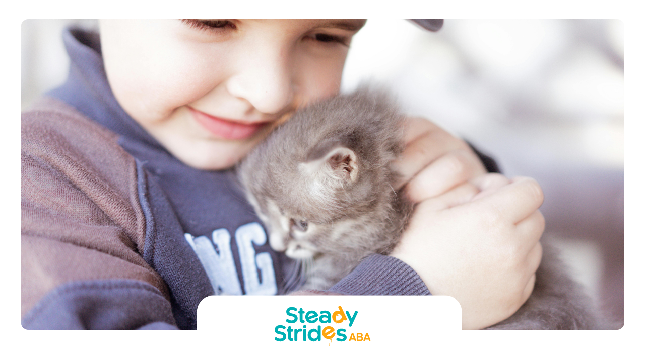 Boy cuddling a gray kitten, both smiling.