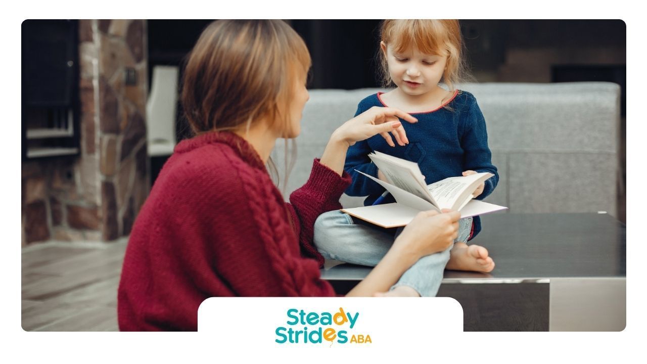A BCBA and a little girl are sitting at a table reading a book.