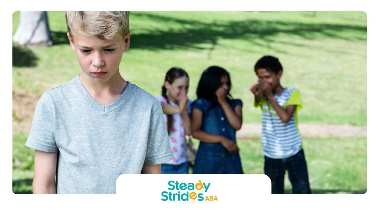 A sad boy with autism stands alone while others laugh in the background