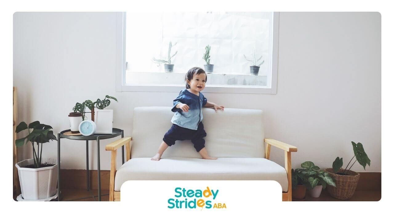 An autistic toddler is standing on a couch in a living room.