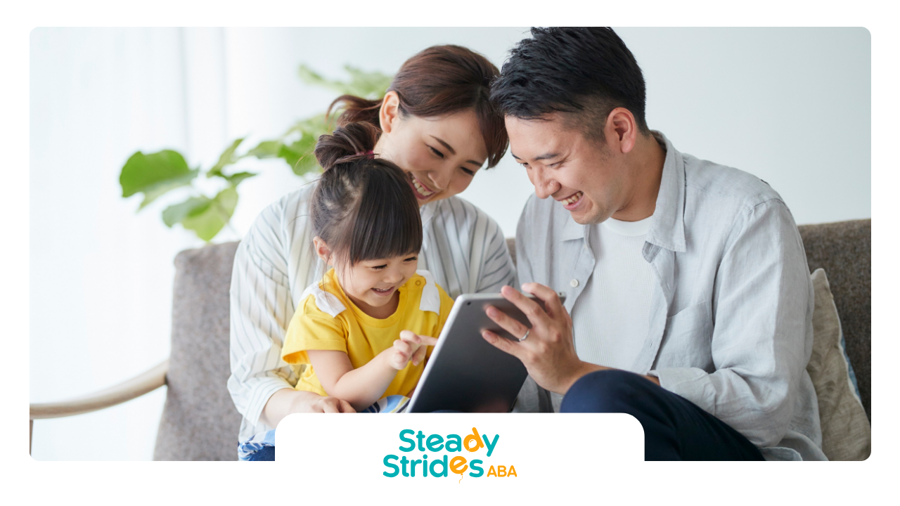 Family of three smiles while looking at a tablet together indoors.