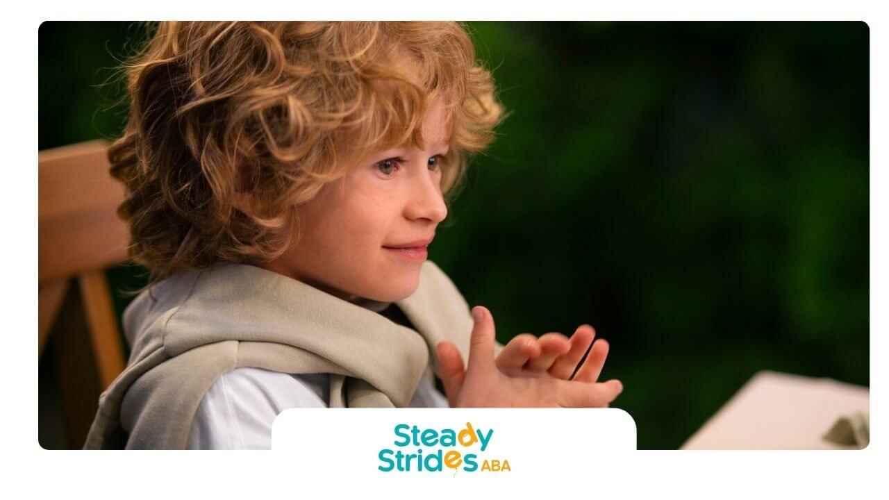 Autistic boy with curly hair is sitting at a table, concentrating on a task with his hands.