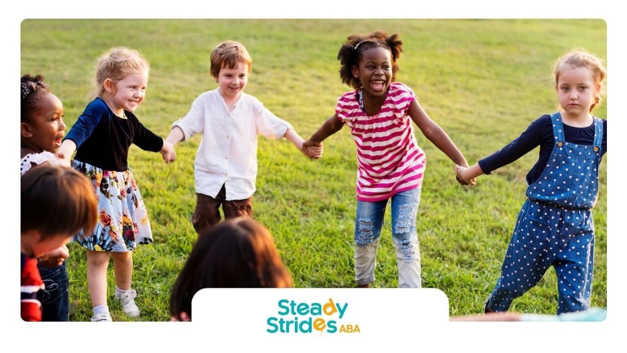 Group of children with autism holding hands and playing together in a grassy park.