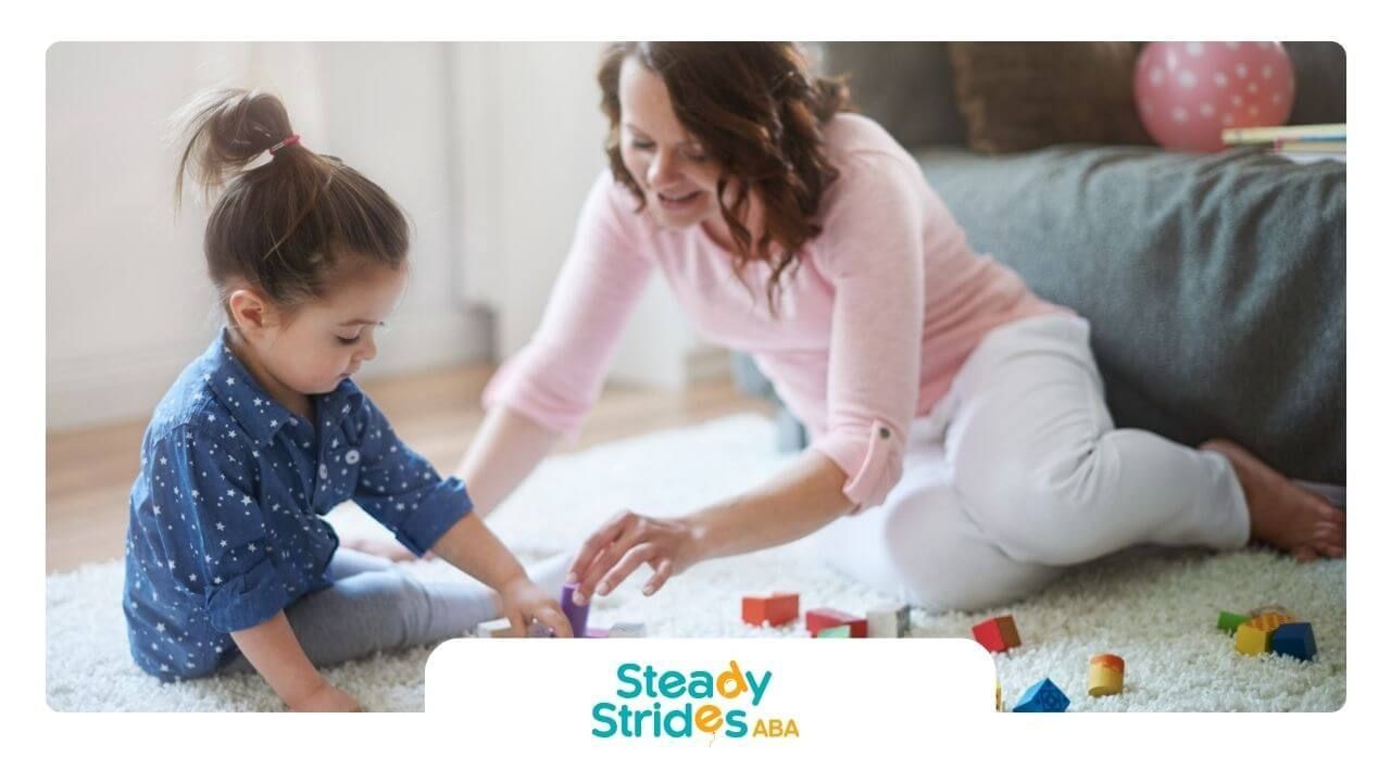 A BCBA and a little girl are playing with blocks on the floor in ABA therapy.