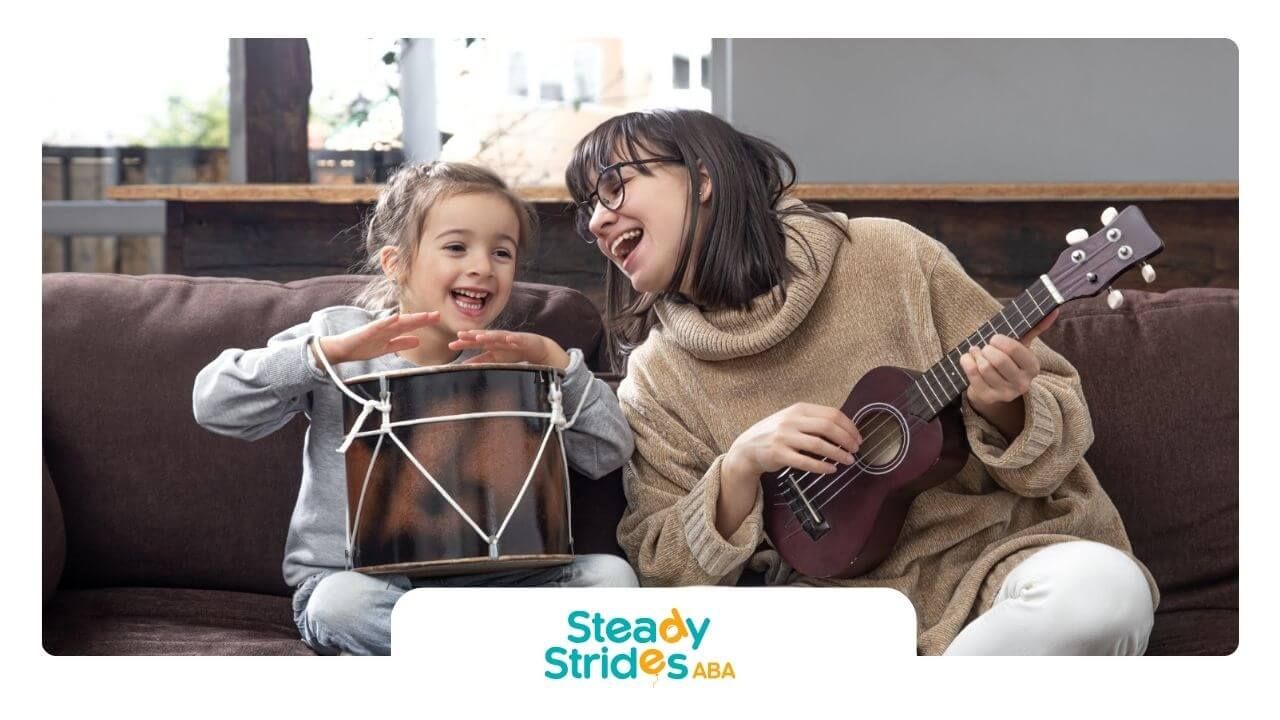 BCBA playing ukulele and little girl playing drum together on a couch in ABA therapy.