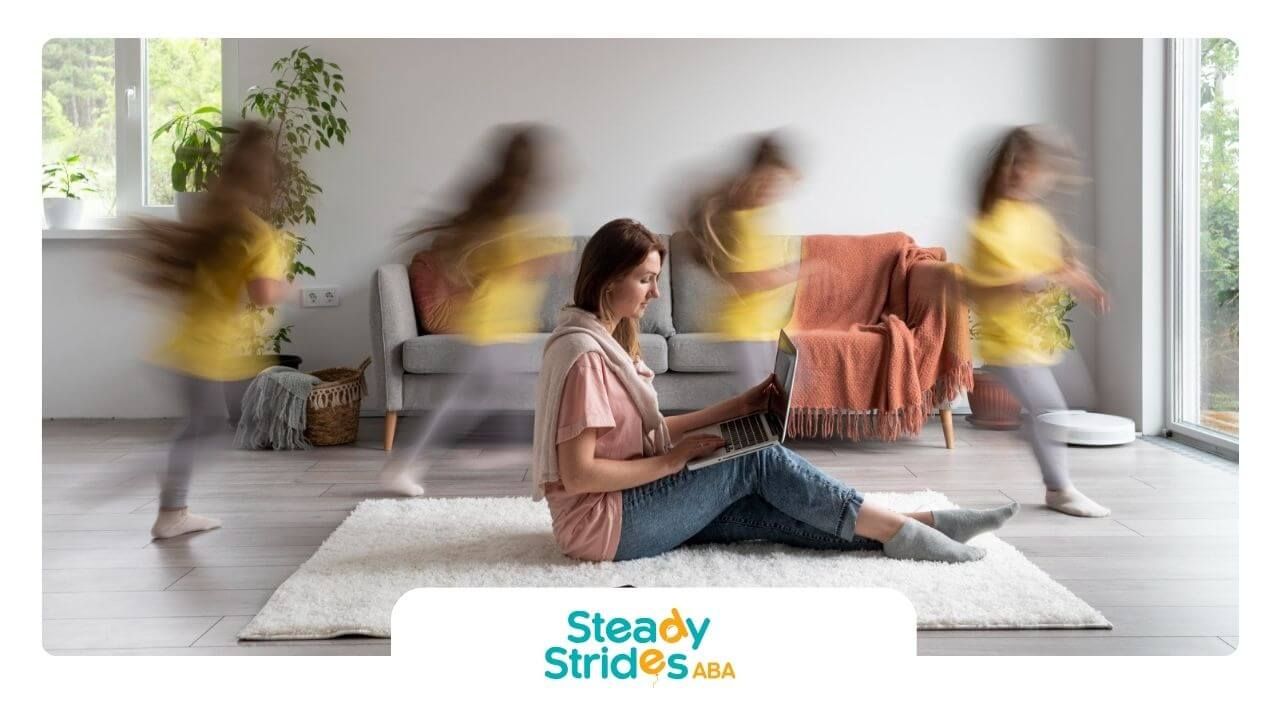 BCBA sitting on the floor using a laptop while children with autism run around her.