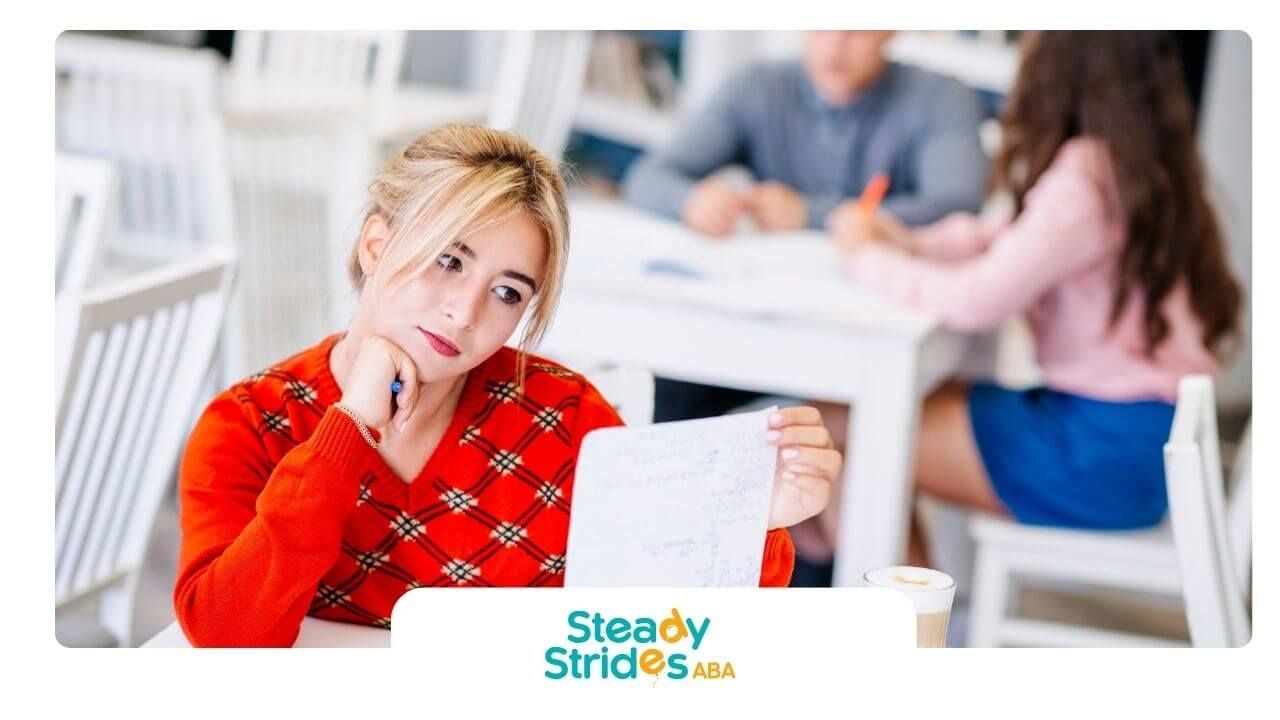 ABA student reviewing notes in a classroom, looking thoughtful while studying with classmates.