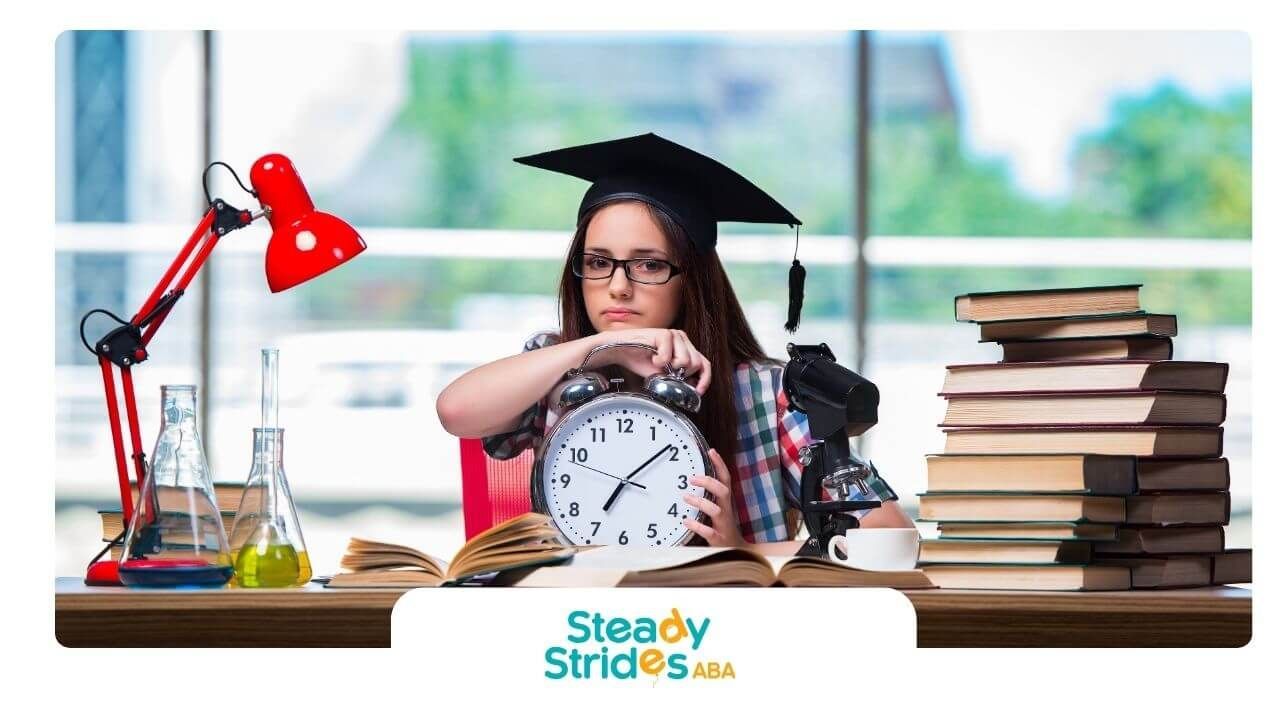 A therapist wearing a graduation cap sits at a desk with books, a clock, and study materials