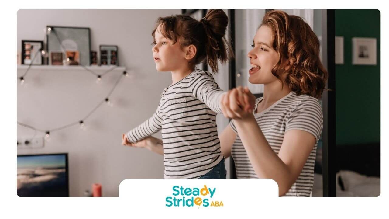 ABA therapist helping autistic daughter balance & stretch arms during playful movement activity.