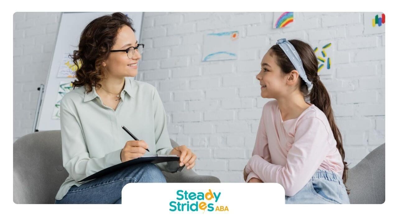 A BCBA is talking to a little girl while holding a pen during ABA therapy.