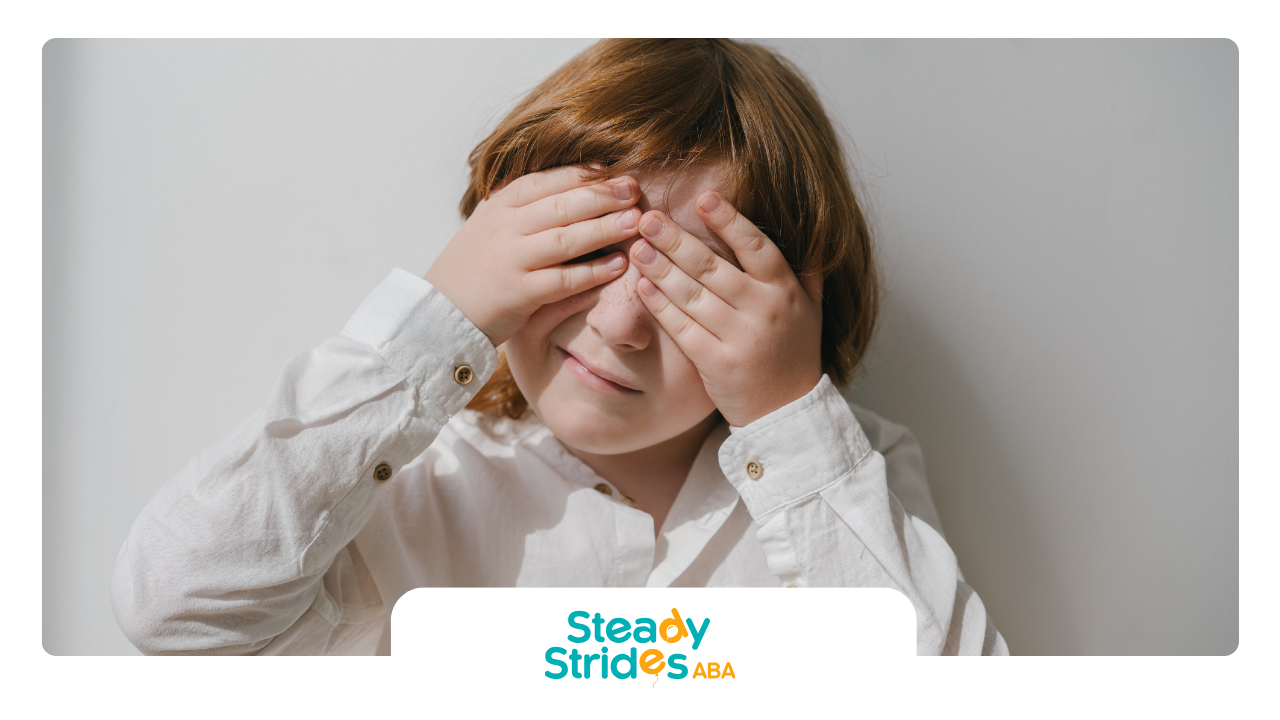 Boy with red hair covers eyes with hands against a white wall.