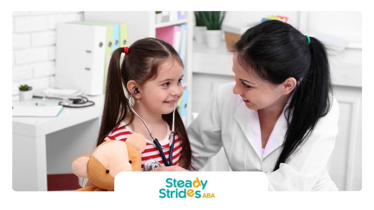 Female doctor using a stethoscope with a smiling girl with autism holding a teddy bear.