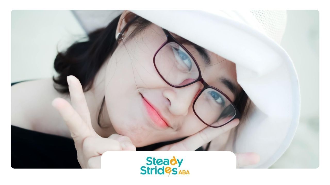 Autistic woman smiling and making peace signs while wearing glasses and a white hat in Texas.