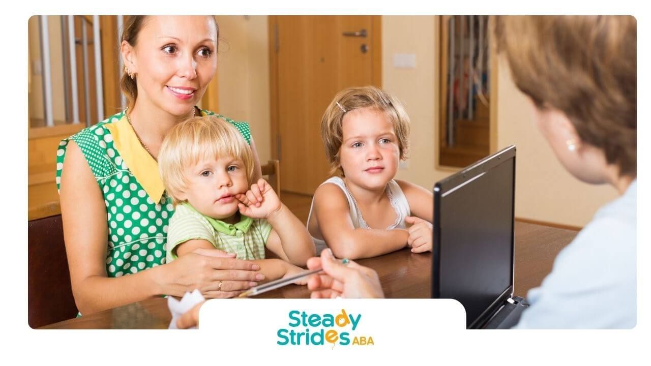 Mother with two autistic children meeting a professional at a desk, discussing services indoor