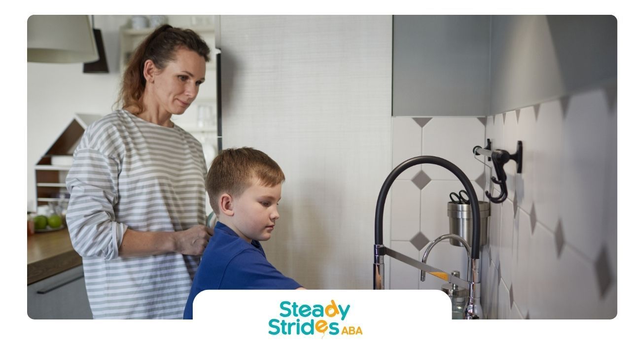 Woman watches a child wash hands at a kitchen sink.
