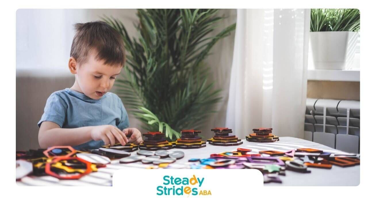Autistic boy playing with colorful puzzle pieces on a table, focusing on stacking & sorting shapes.