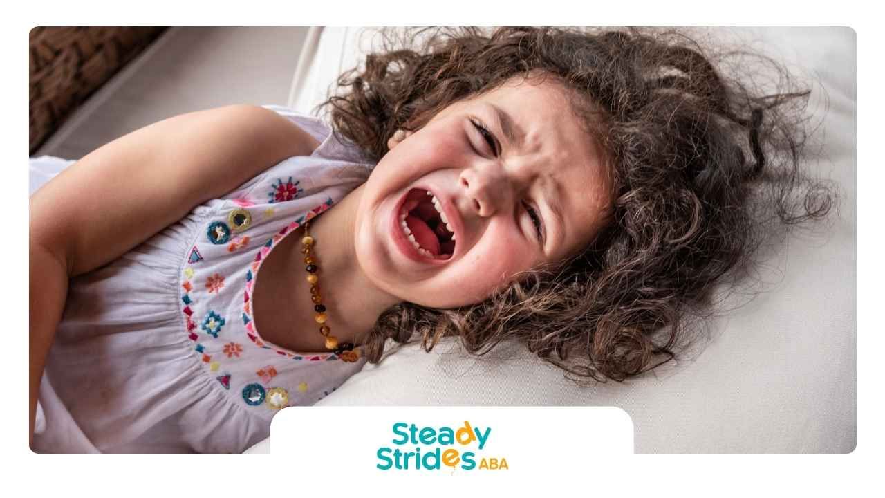 A young child with curly hair is lying down, visibly crying. 