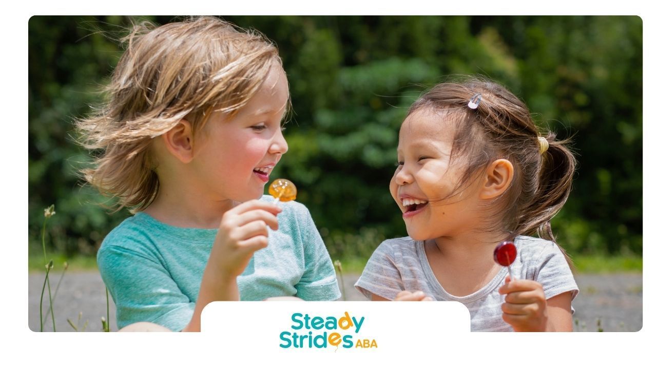 Two children smiling and holding lollipops outdoors.