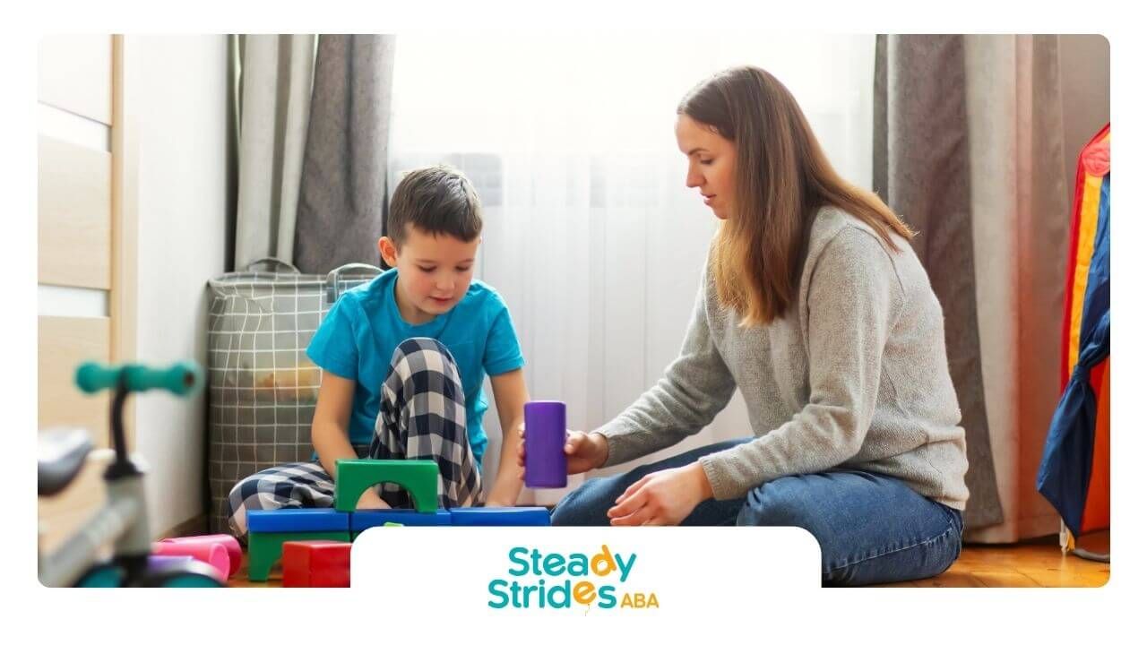 A BCBA and a boy are playing with blocks in a room in ABA therapy.
