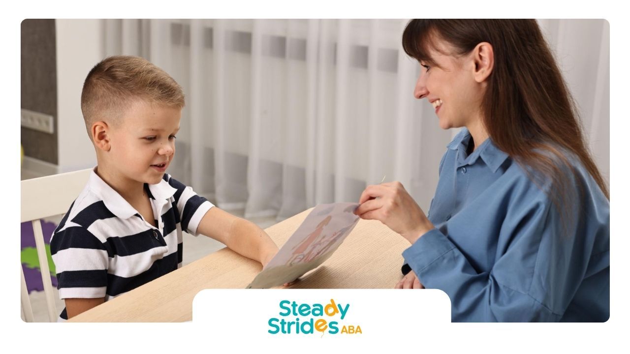 A BCBA is talking to a young boy who is sitting at a table.