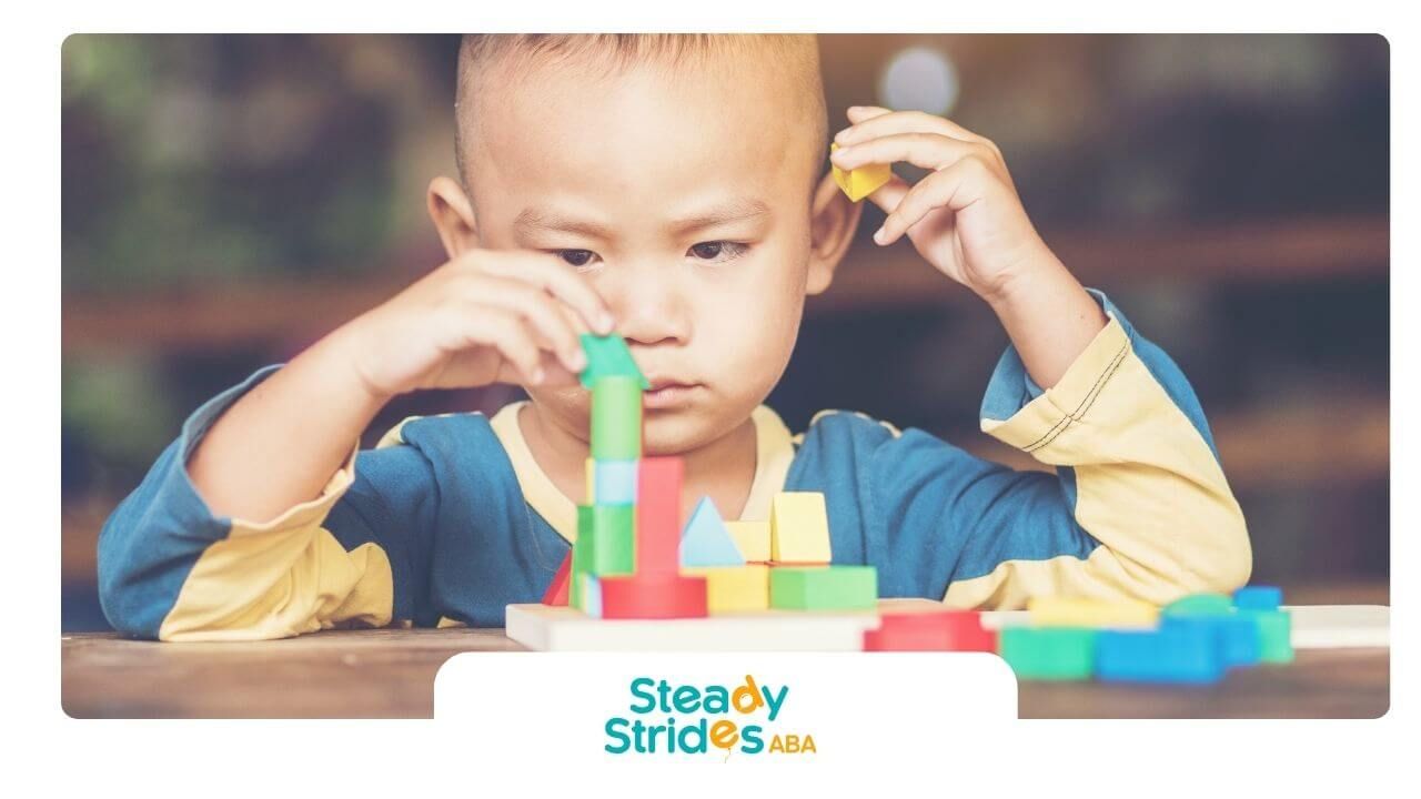 Autistic toddler concentrating while stacking colorful blocks, developing focus and motor skills.