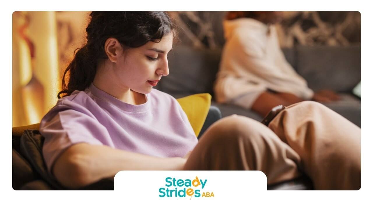 Teen girl with autism sitting alone indoors looking down.