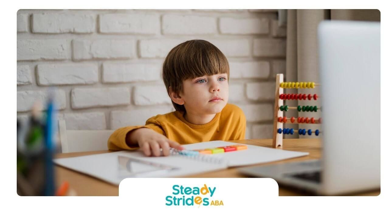 Autistic child works with counting blocks and abacus while focusing on learning activities at a desk