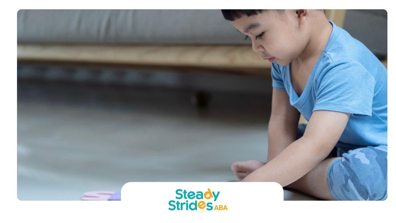 Autistic boy sitting on floor arranging colorful foam letters during early learning activity.