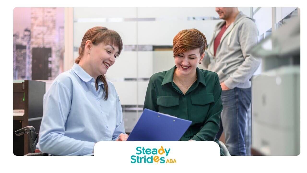 Two autistic women smiling and reviewing documents together in an office while a man stands behind.