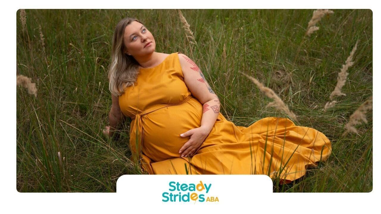 An ABA pregnant woman lies on the ground in a mustard dress, enjoying nature while looking up.