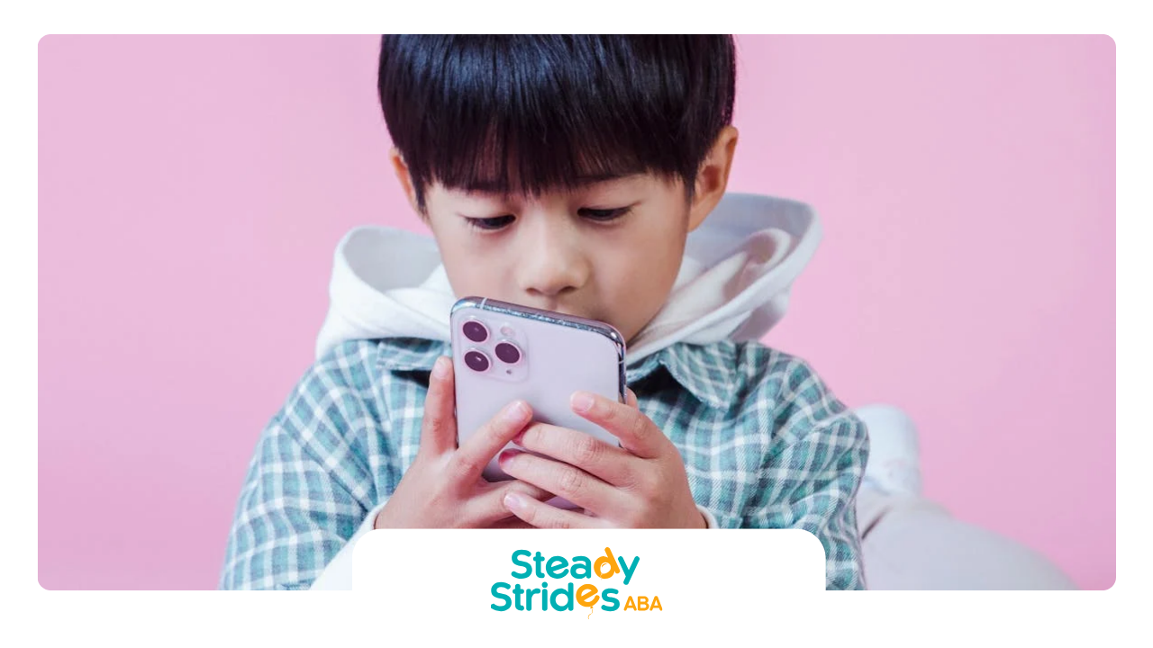 Boy looking intently at a smartphone, hands on device, pink background.