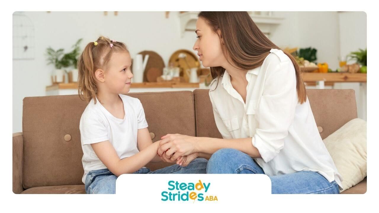 ABA therapist holding hands and talking with a young girl on a sofa in ABA therapy. 