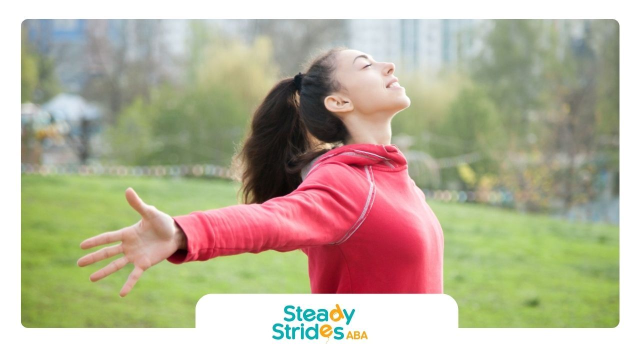 An autistic woman in Texas is standing in a park with her arms outstretched.